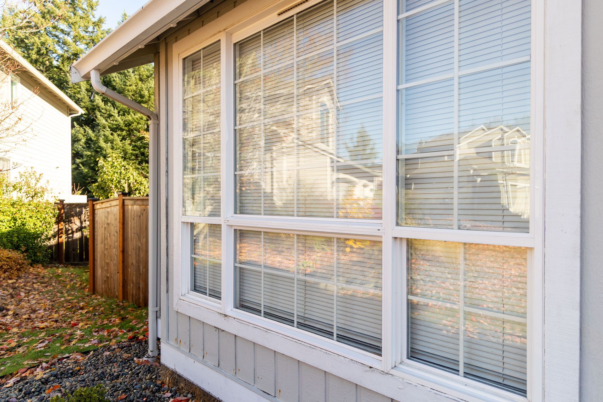A clean residential window with closed blinds overlooks a small, well-maintained yard.