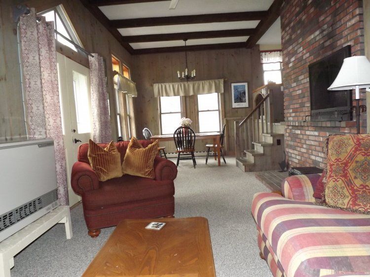 Cozy living room with exposed brick walls, red chairs, striped sofa, and a wooden coffee table.