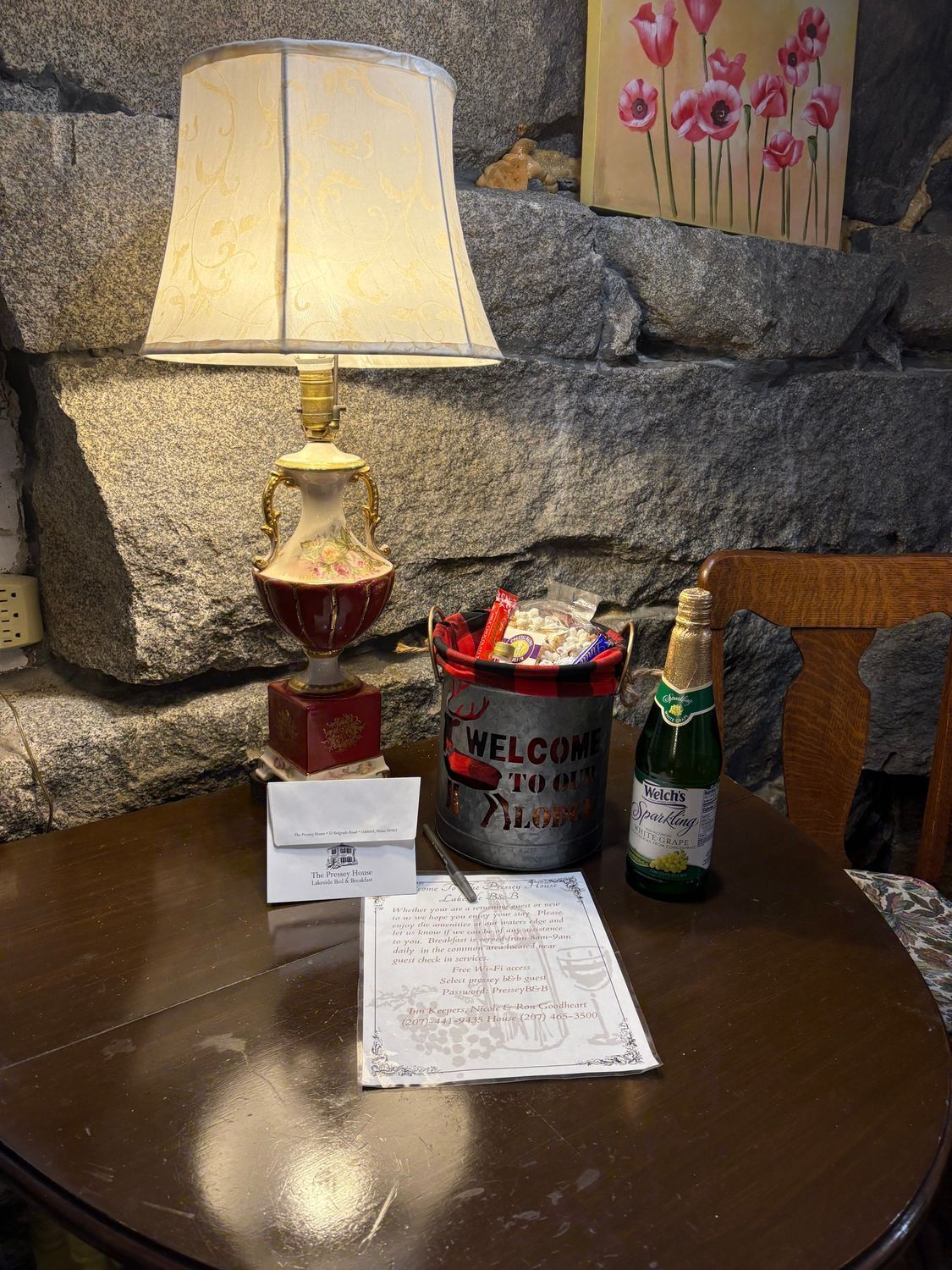 Table lamp, mug, and beer bottle on a dark wooden table by a stone wall.