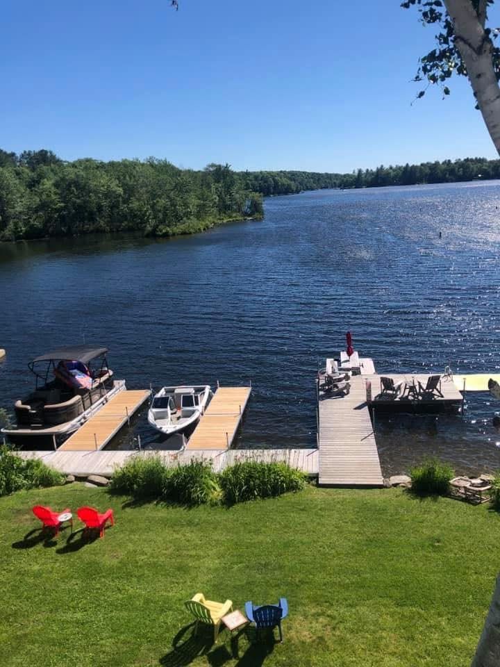 Lakefront dock with boats, red chairs on a green lawn, and calm blue water under a clear sky