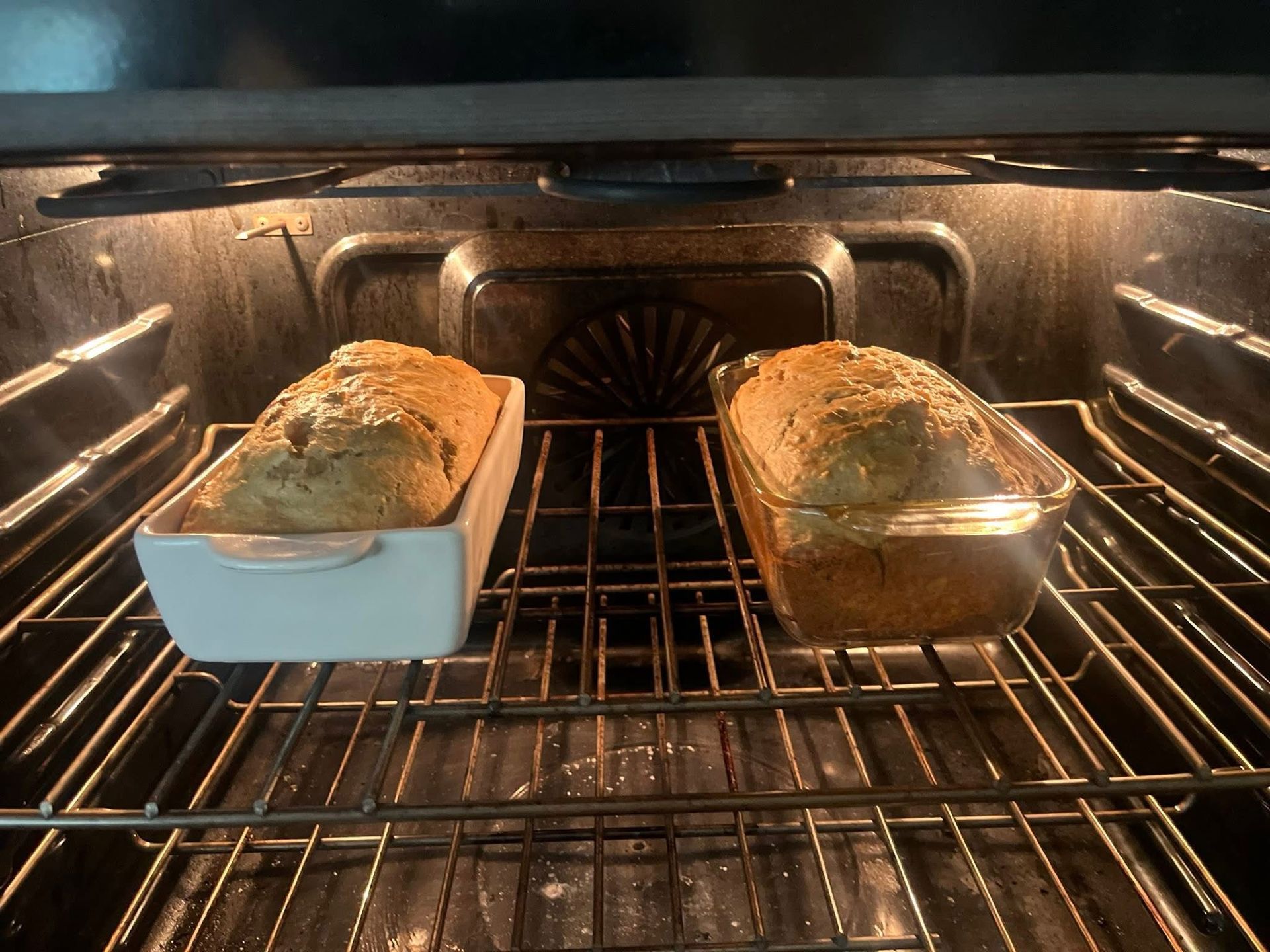 Two loaf pans of bread baking in an oven, tops golden brown
