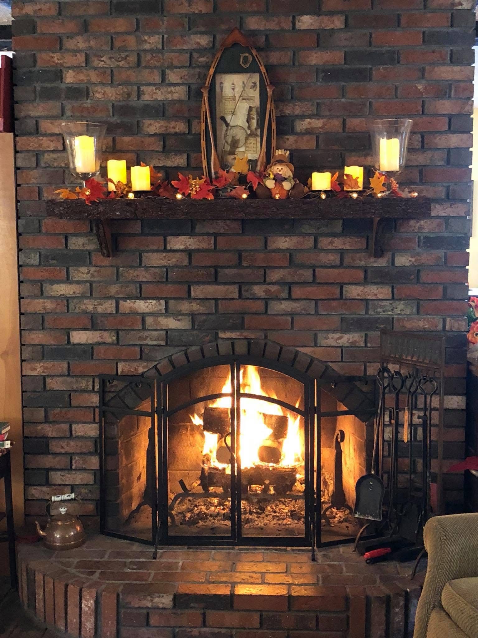 Brick fireplace with a lit fire, candles on the mantel, and a decorative mirror above it.
