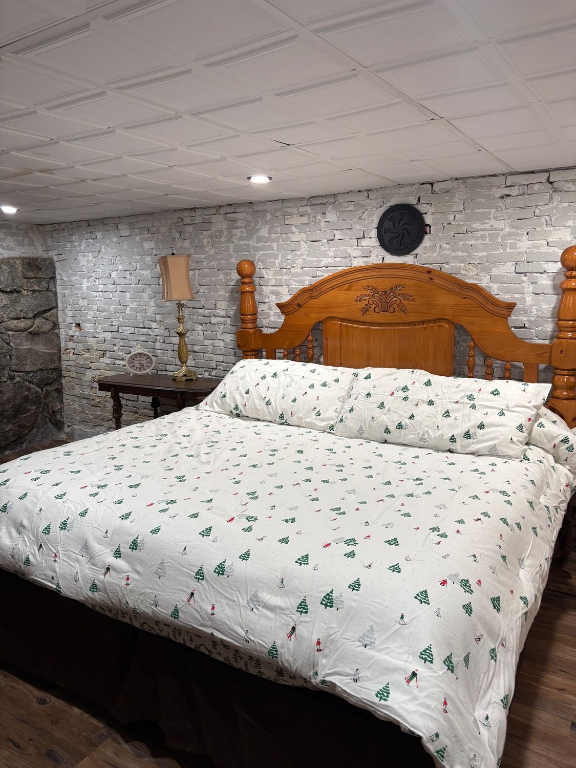 Cozy bedroom with a wooden bed, floral bedding, stone accent wall, and lamp under a white ceiling