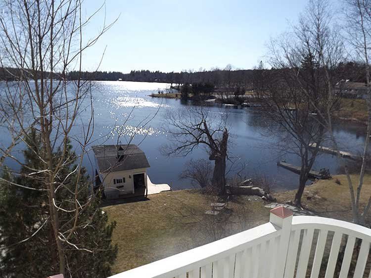 Snowy lakeside view with bare trees, a small shed, and sunlight reflecting on the water