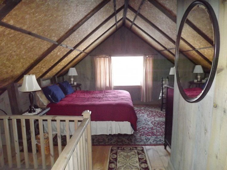 Loft bedroom with wood-beamed ceiling, red bedspread, patterned rug, and window curtains