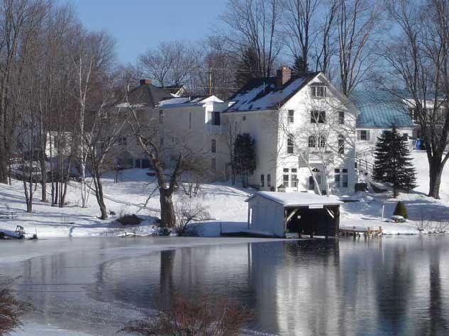 Snowy lakeside house with dock and bare trees reflected in calm water