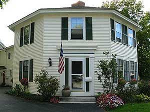 White two-story house with black shutters, front porch, American flag, and flower beds