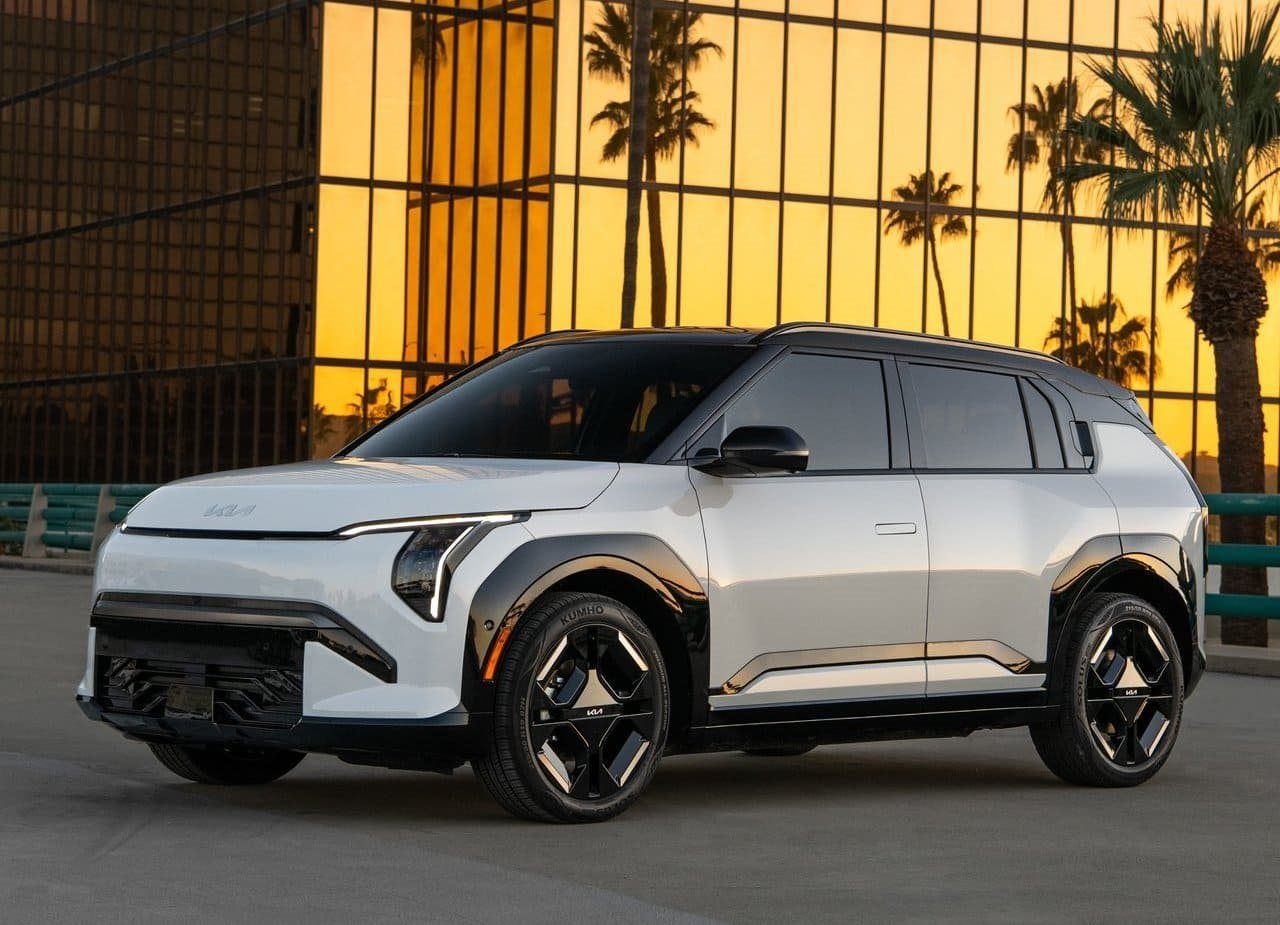 White futuristic SUV parked outdoors at sunset, with black wheels and palm trees in the background