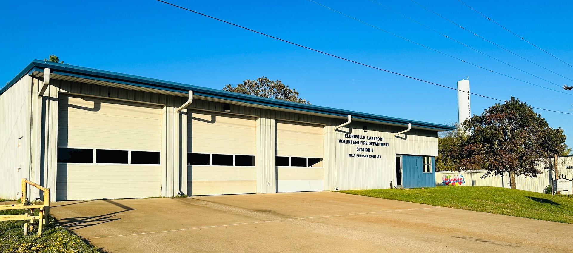 A large white building with a lot of garage doors is sitting on top of a dirt field.
