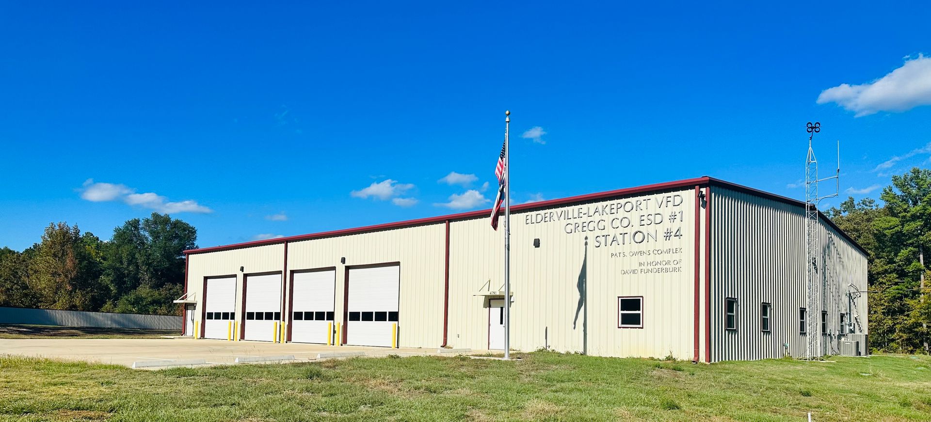 A large white building with a red roof is sitting in the middle of a grassy field.