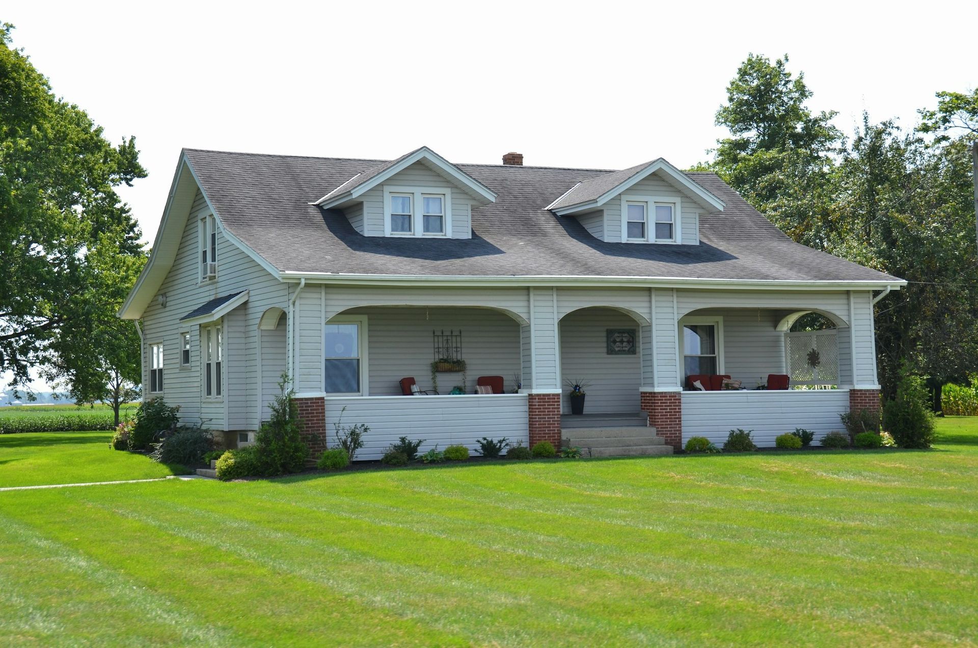 A rural American farmhouse with a covered porch on a wide mown lawn beside a field