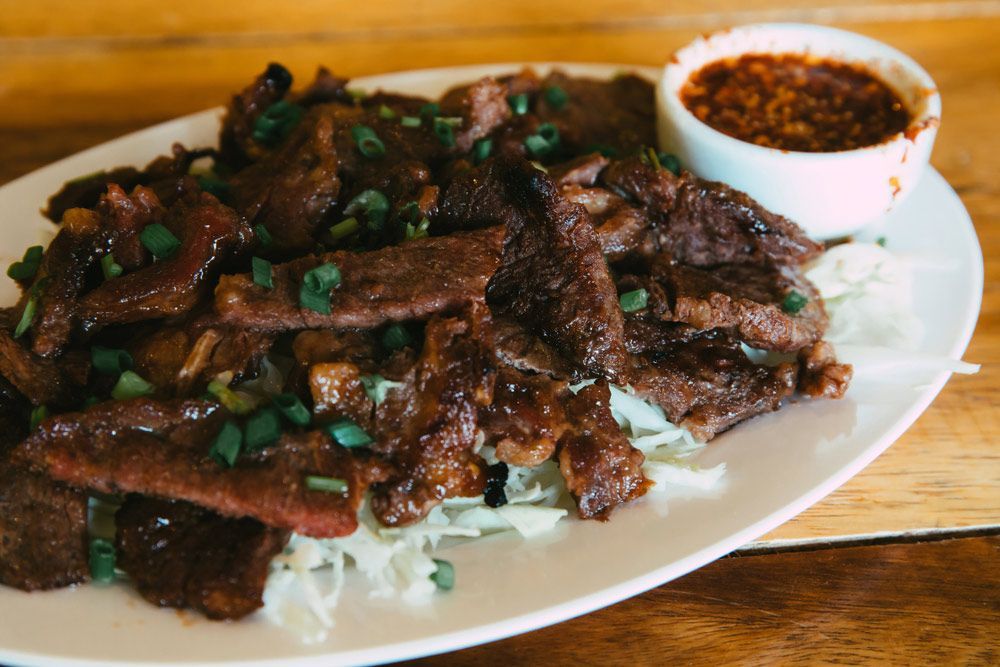 A White Plate Topped With Meat And Cabbage Next To A Small Bowl Of Dipping Sauce — One Thai Cuisine & Noodle Bar In Kirwan, QLD