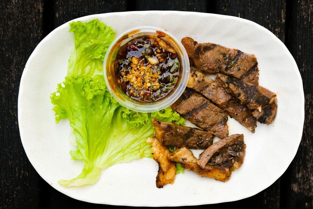 A White Plate Topped With Meat Lettuce And Sauce — One Thai Cuisine & Noodle Bar In Kirwan, QLD