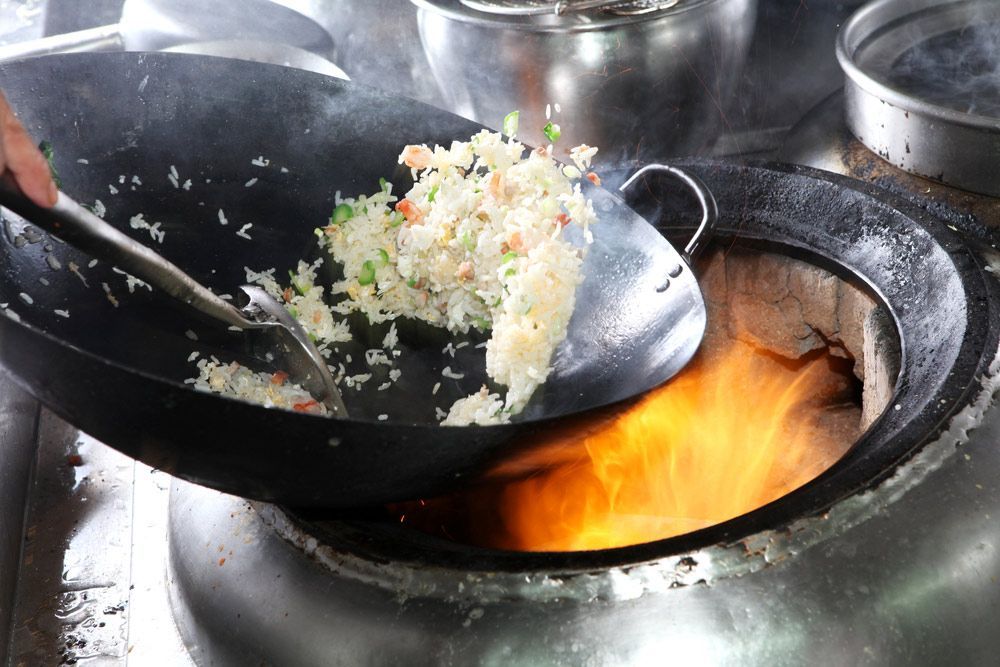 A Person Is Cooking Rice In A Wok Over A Fire — One Thai Cuisine & Noodle Bar In Kirwan, QLD