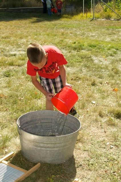 A young boy is pouring water into a metal tub.