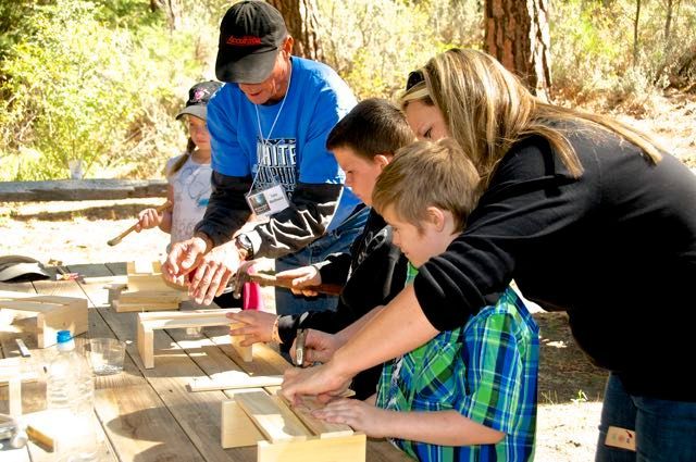 A group of people are working on wooden blocks at a picnic table.