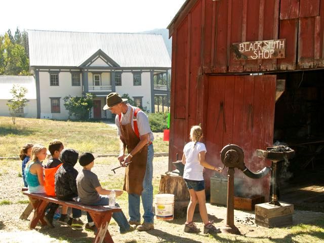 A group of children sit on a bench in front of a blacksmith shop