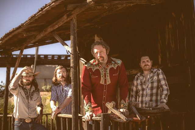 A group of men are standing in front of a wooden building.