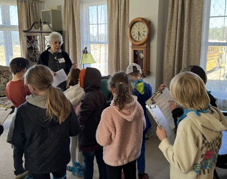 A woman is talking to a group of children in a living room.