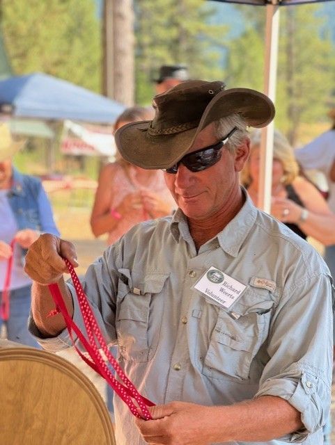 A man wearing a cowboy hat and sunglasses is holding a red rope