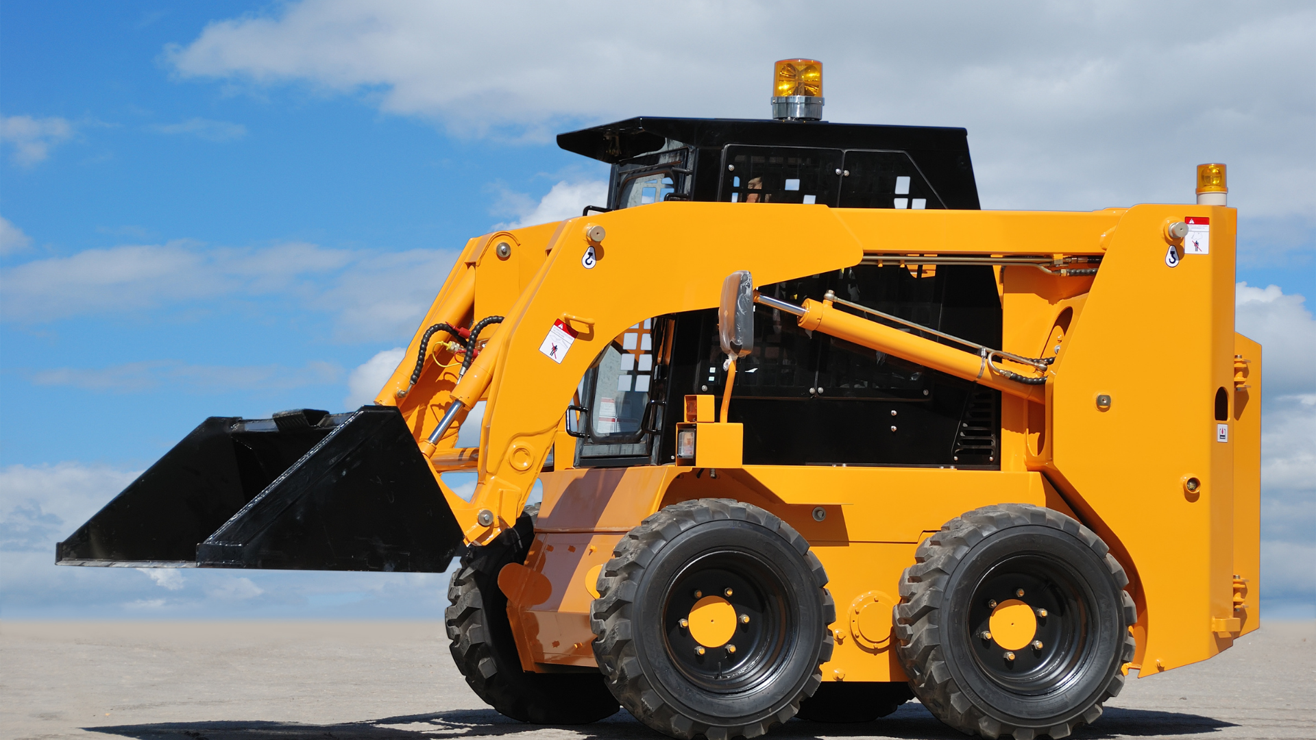 Yellow front-end loader with black bucket on a paved surface under a blue sky