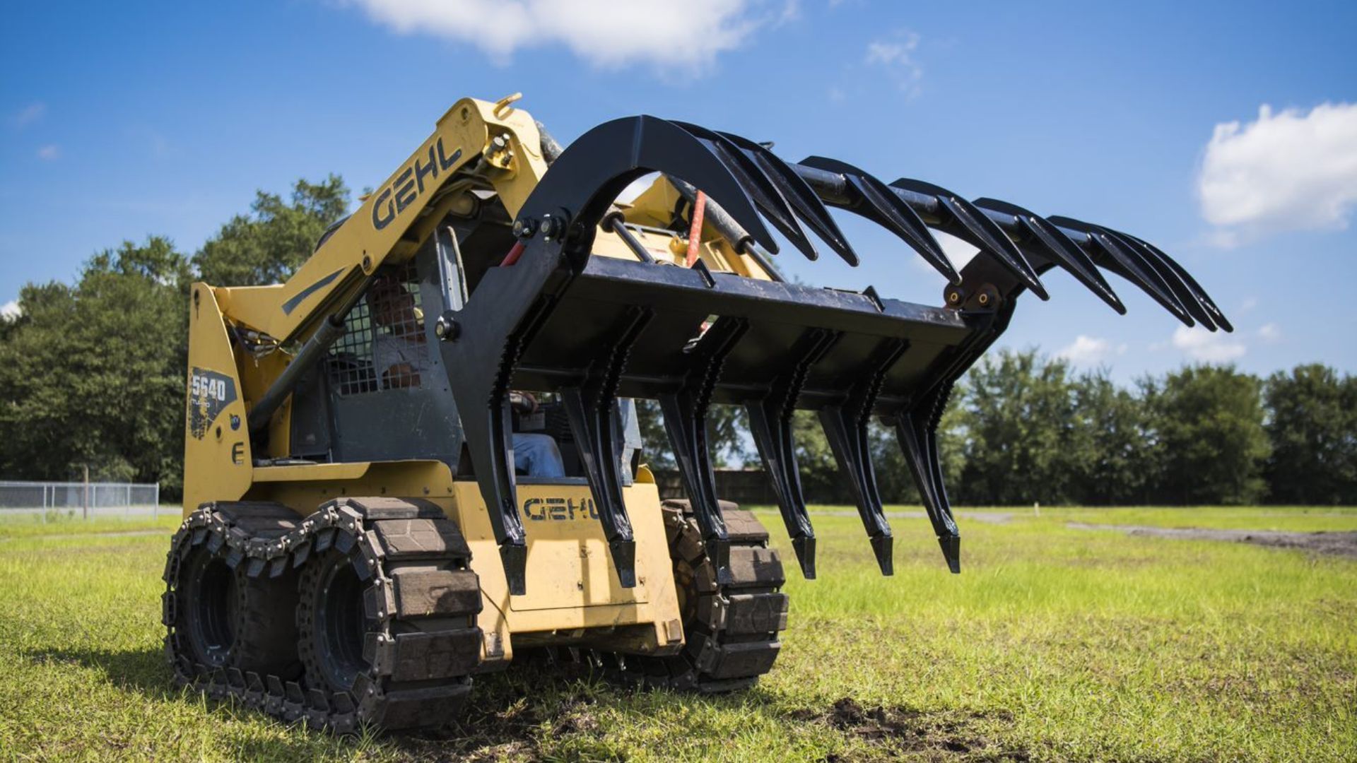 Yellow excavator with large grapple claw parked in a grassy field under a blue sky