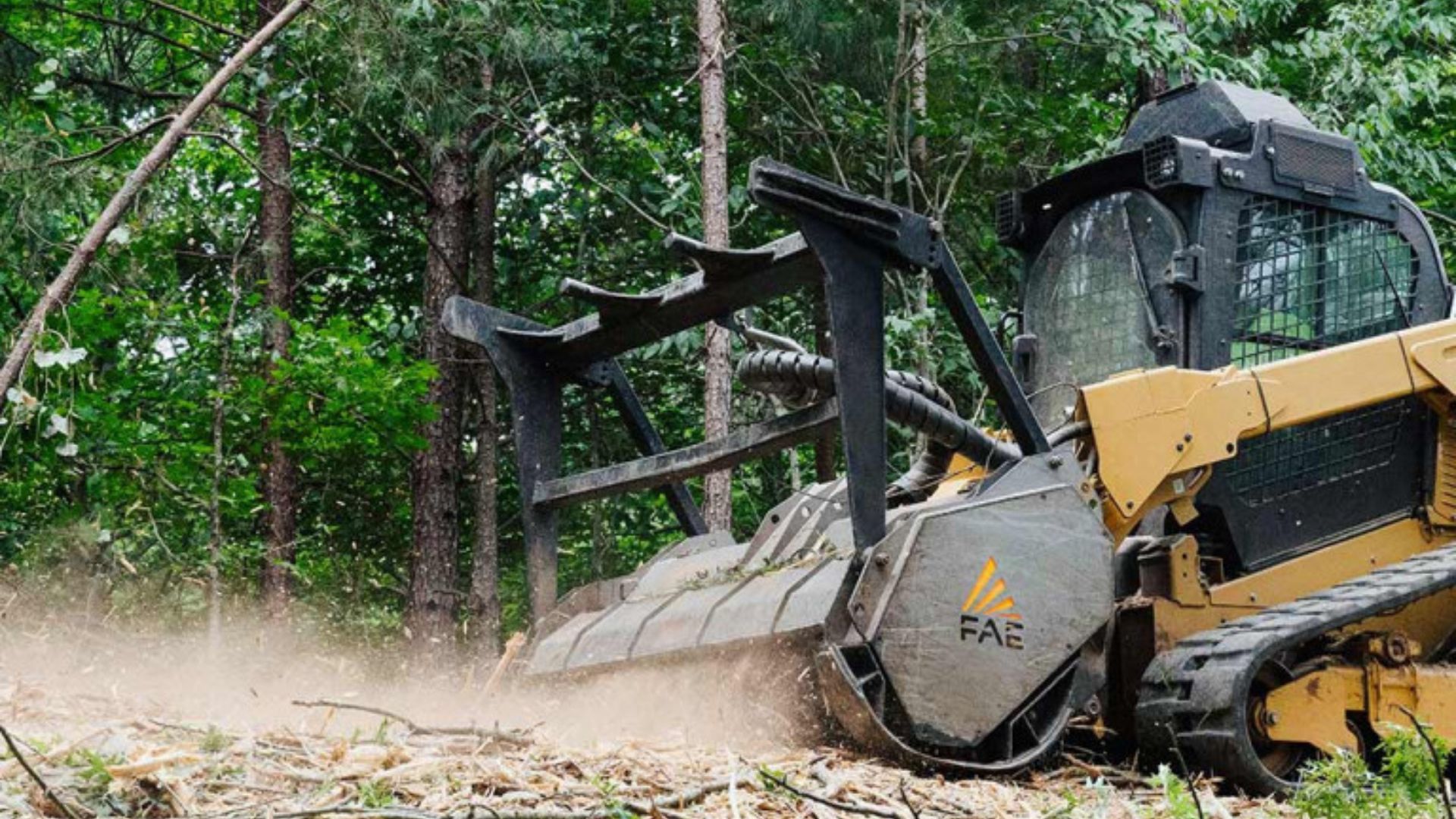 Yellow forestry machine clearing brush in a wooded area, kicking up dust and debris.
