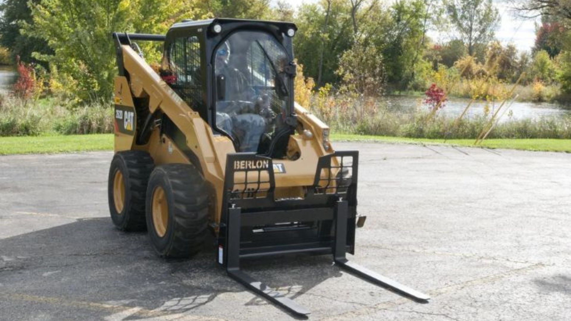 Yellow CAT skid steer with fork attachment parked on pavement outdoors.