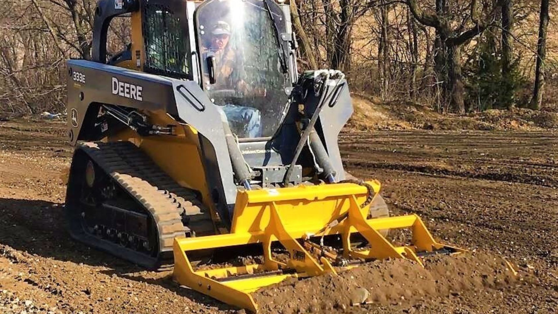 Yellow skid-steer loader clearing dirt in a wooded area on a muddy worksite