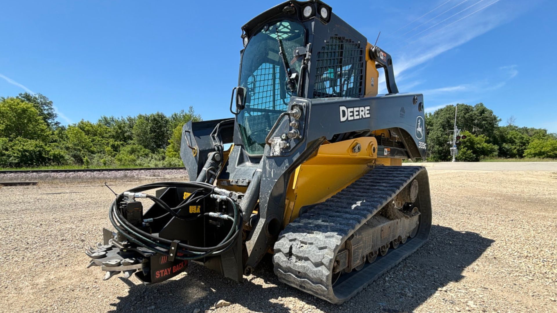 John Deere skid steer with grapple attachment on a gravel lot under a blue sky