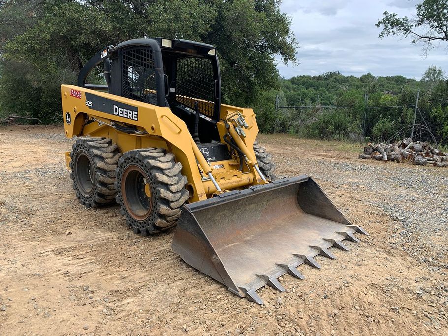 Yellow skid steer loader with raised bucket on a gravel road in a wooded area