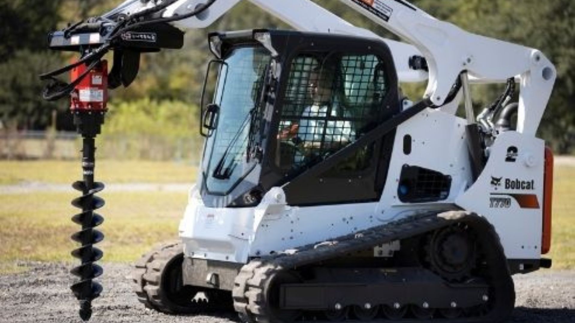 White Bobcat compact track loader drilling a hole with a large auger attachment outdoors