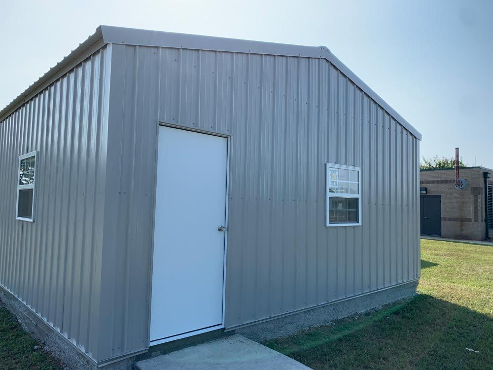 a gray metal shed with a white door and windows .