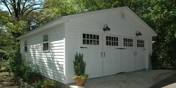a white garage with three doors and windows is surrounded by trees .
