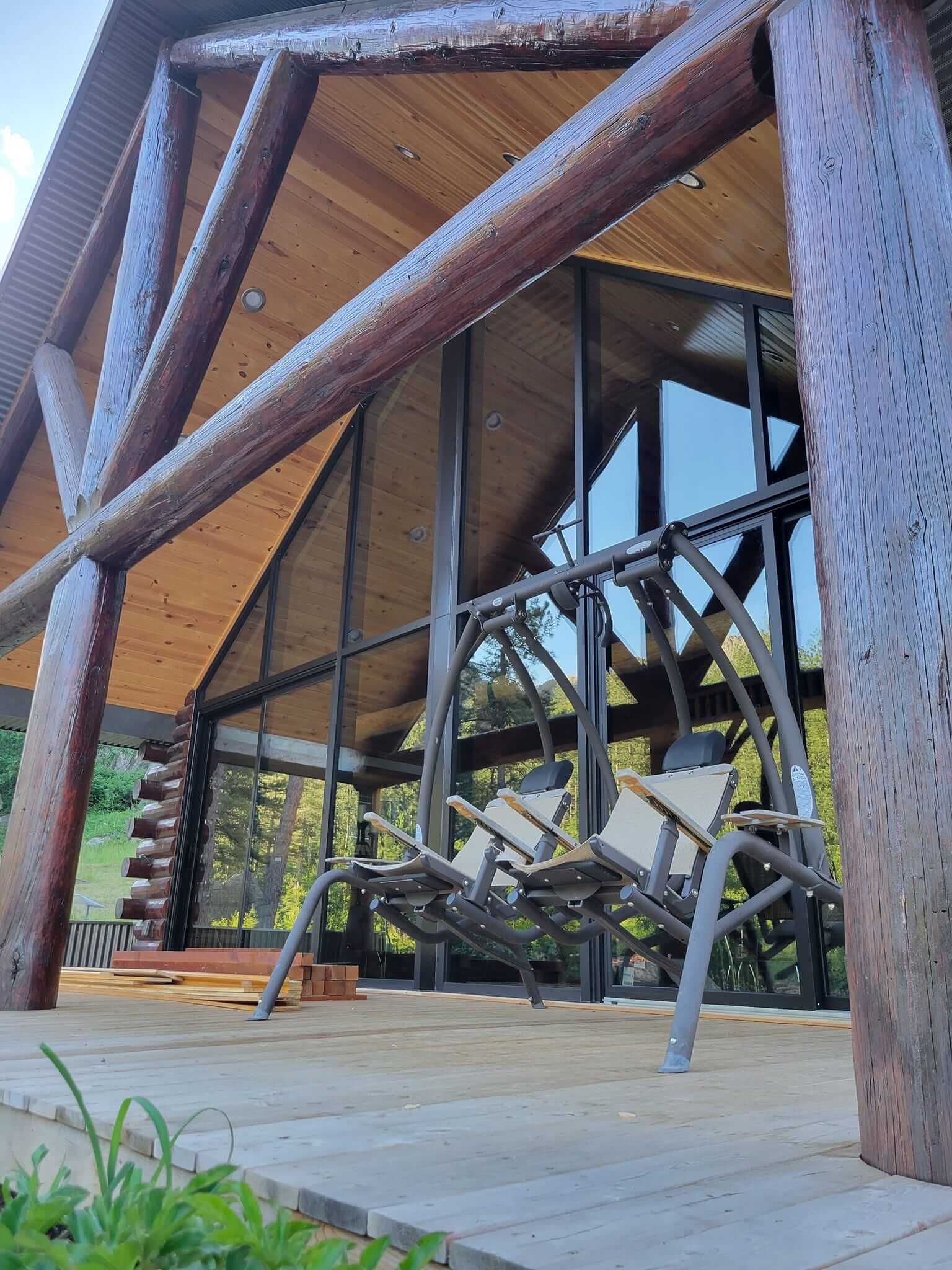A wooden gazebo with a swing and chairs underneath it.