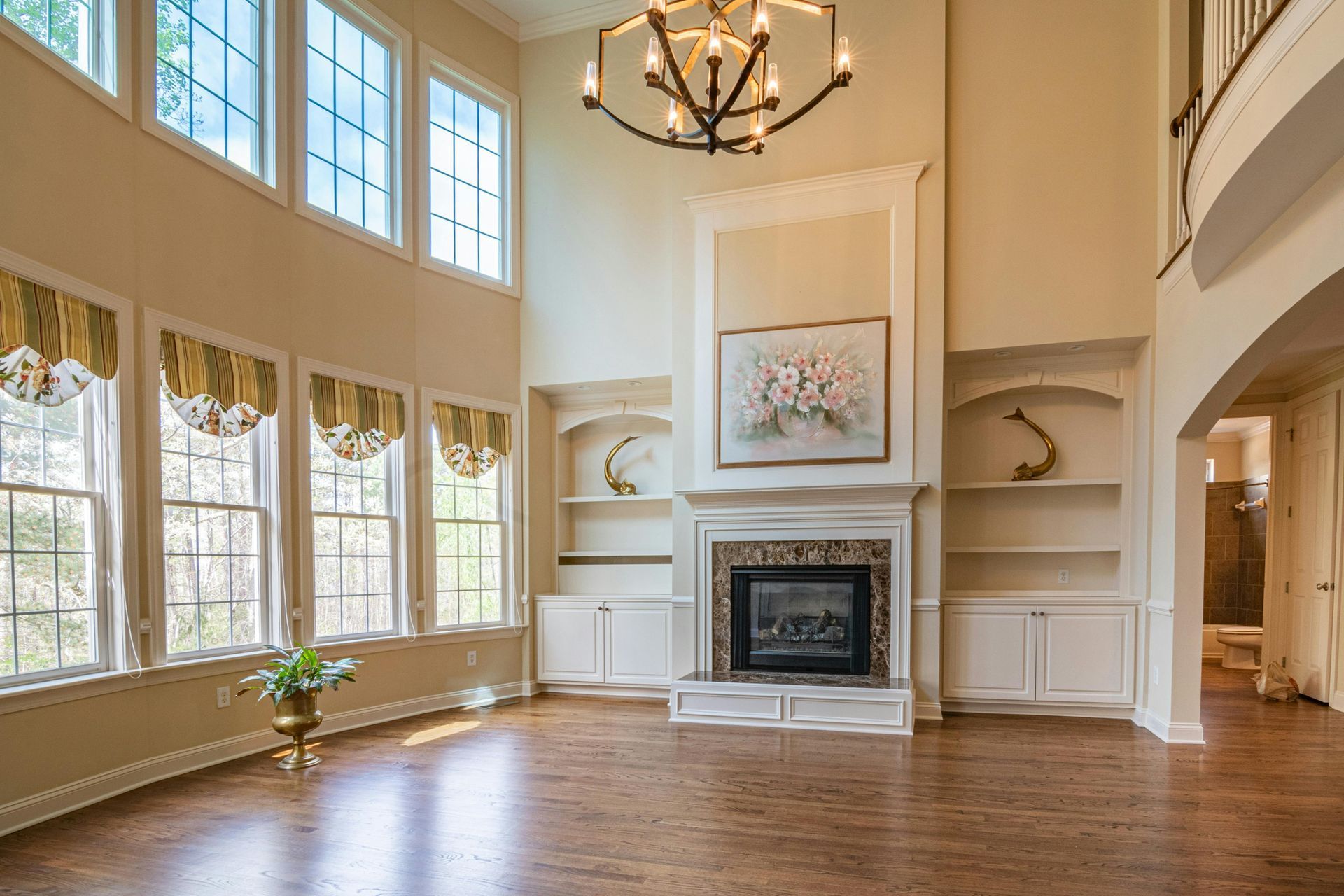 Living room with beige furniture, fireplace, and large windows with cream curtains.