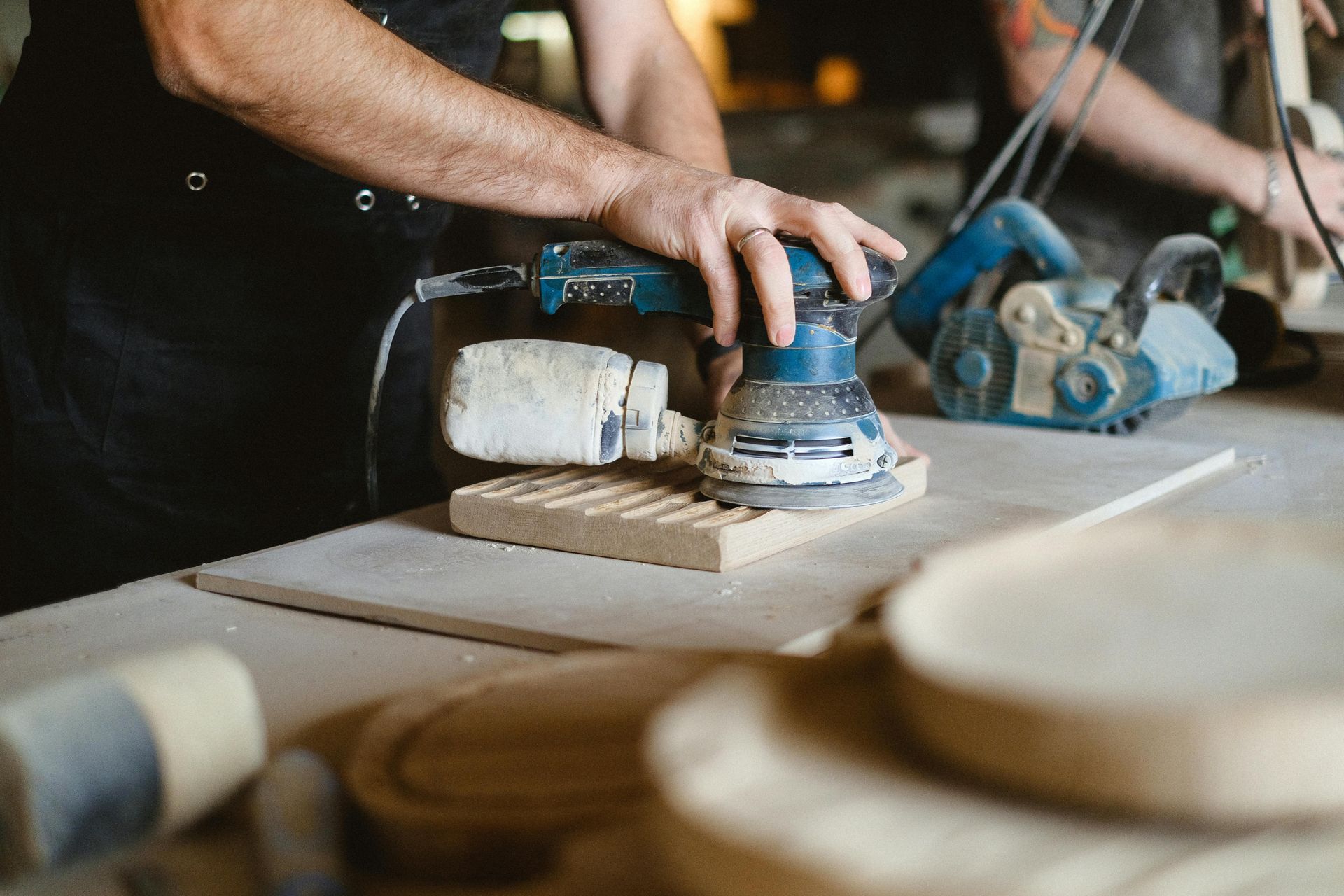 Person sanding a wooden board with a power sander in a workshop