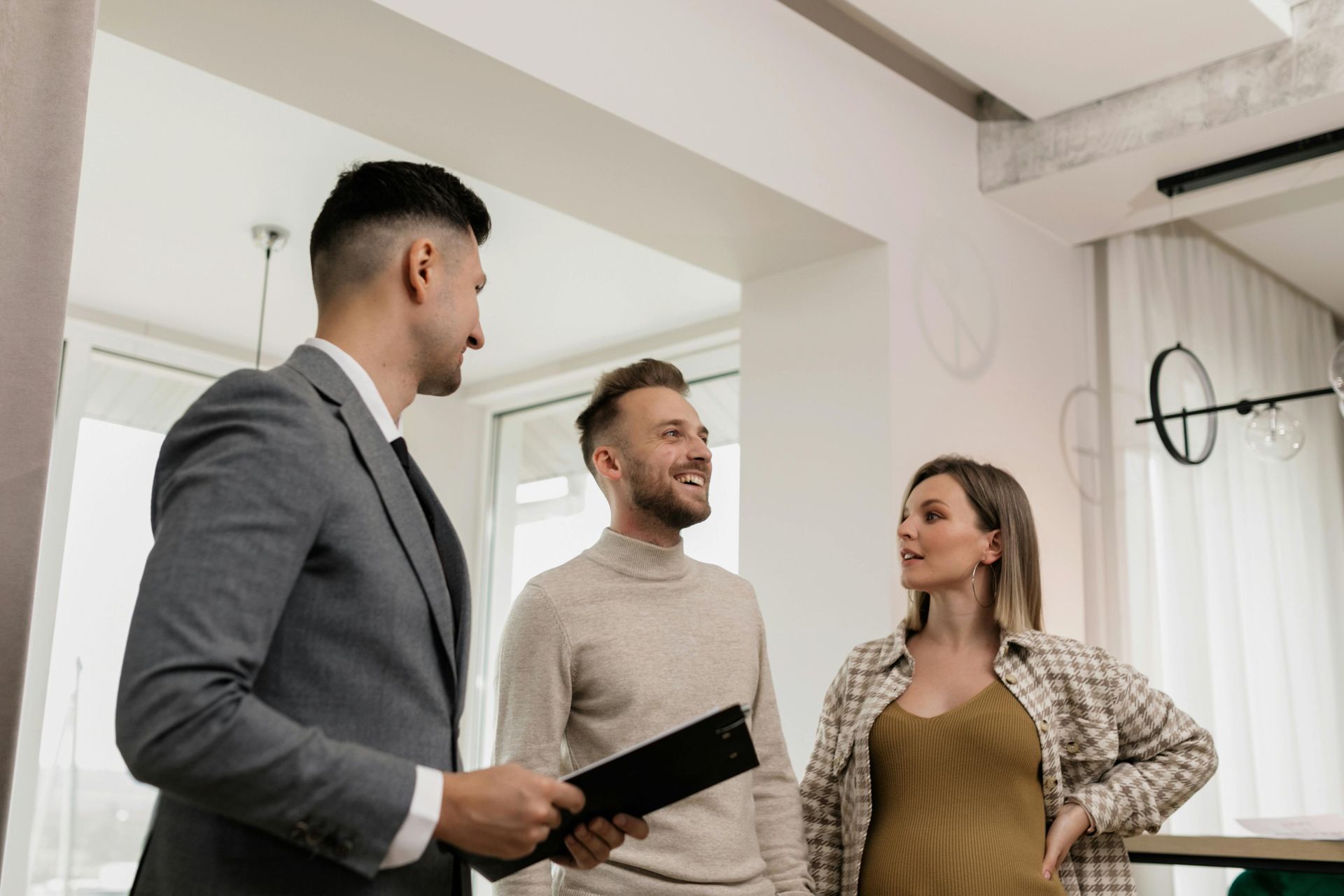 Real estate agent showing a couple a home; interior, daylight. The agent wears a suit, and the couple are smiling.