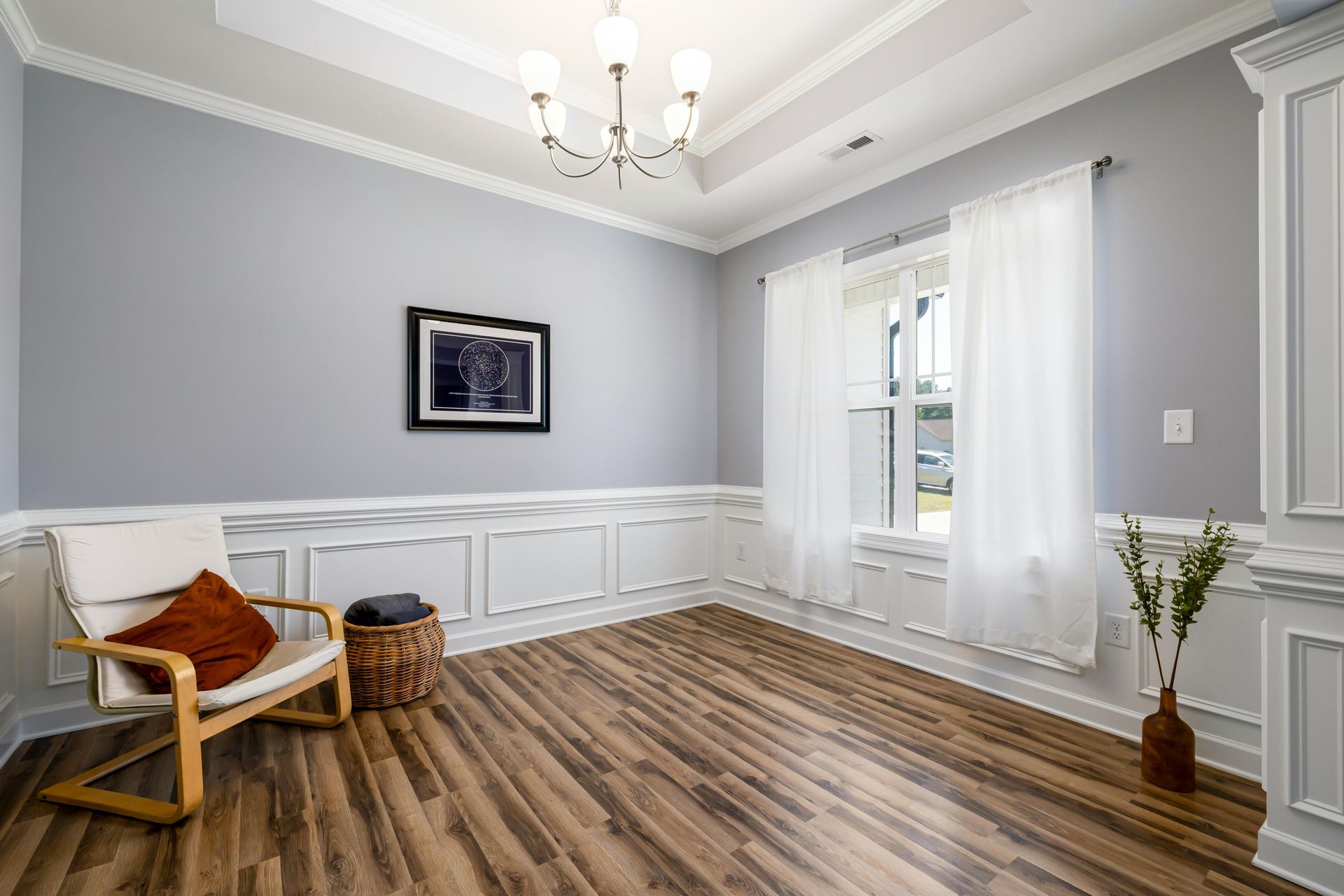 Dining room with light blue walls, wood floors, and white trim. Includes a chair, art, and a vase.