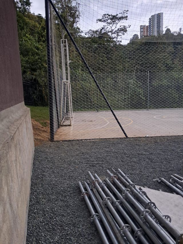Rollos de malla eslabonada galvanizada y postes de acero en un patio industrial.