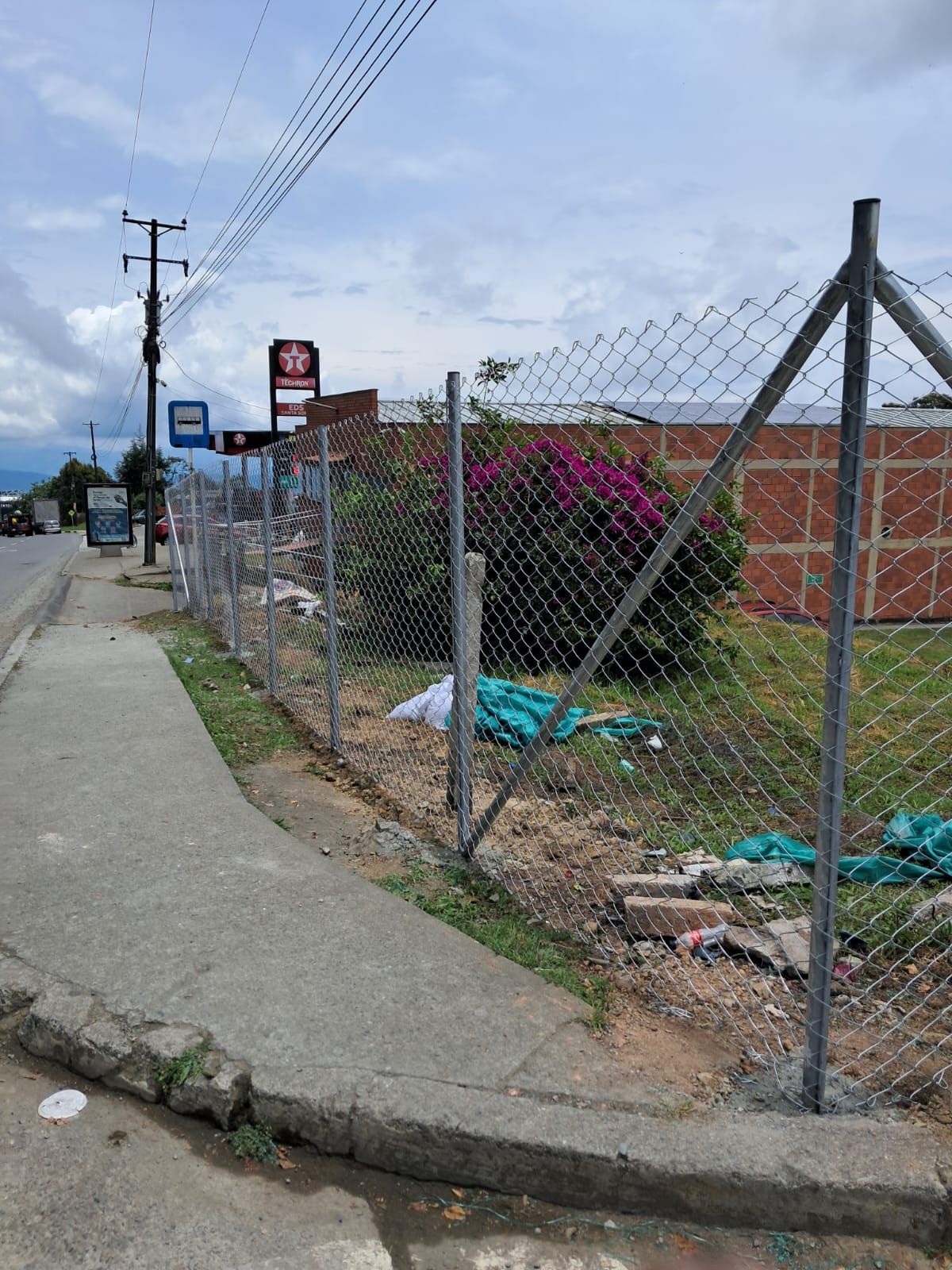 Una valla de tela metálica bordea una acera junto a un terreno baldío