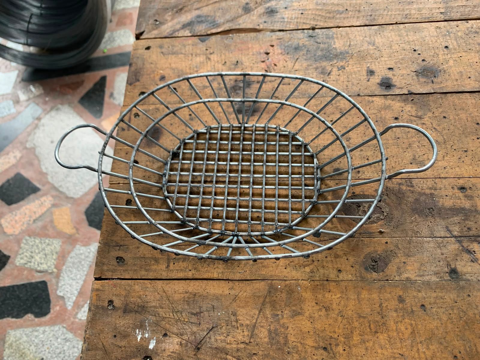 Cesta de alambre para asar con asas sobre una mesa de madera.