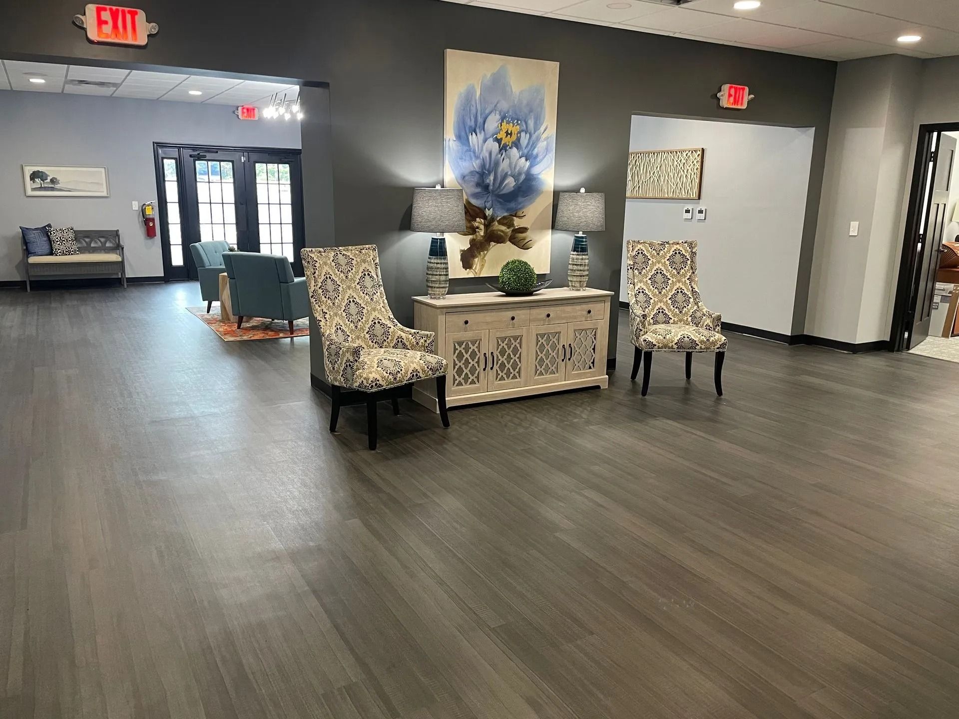 A lobby with hardwood floors, two patterned chairs, a floral artwork, and a white console table.