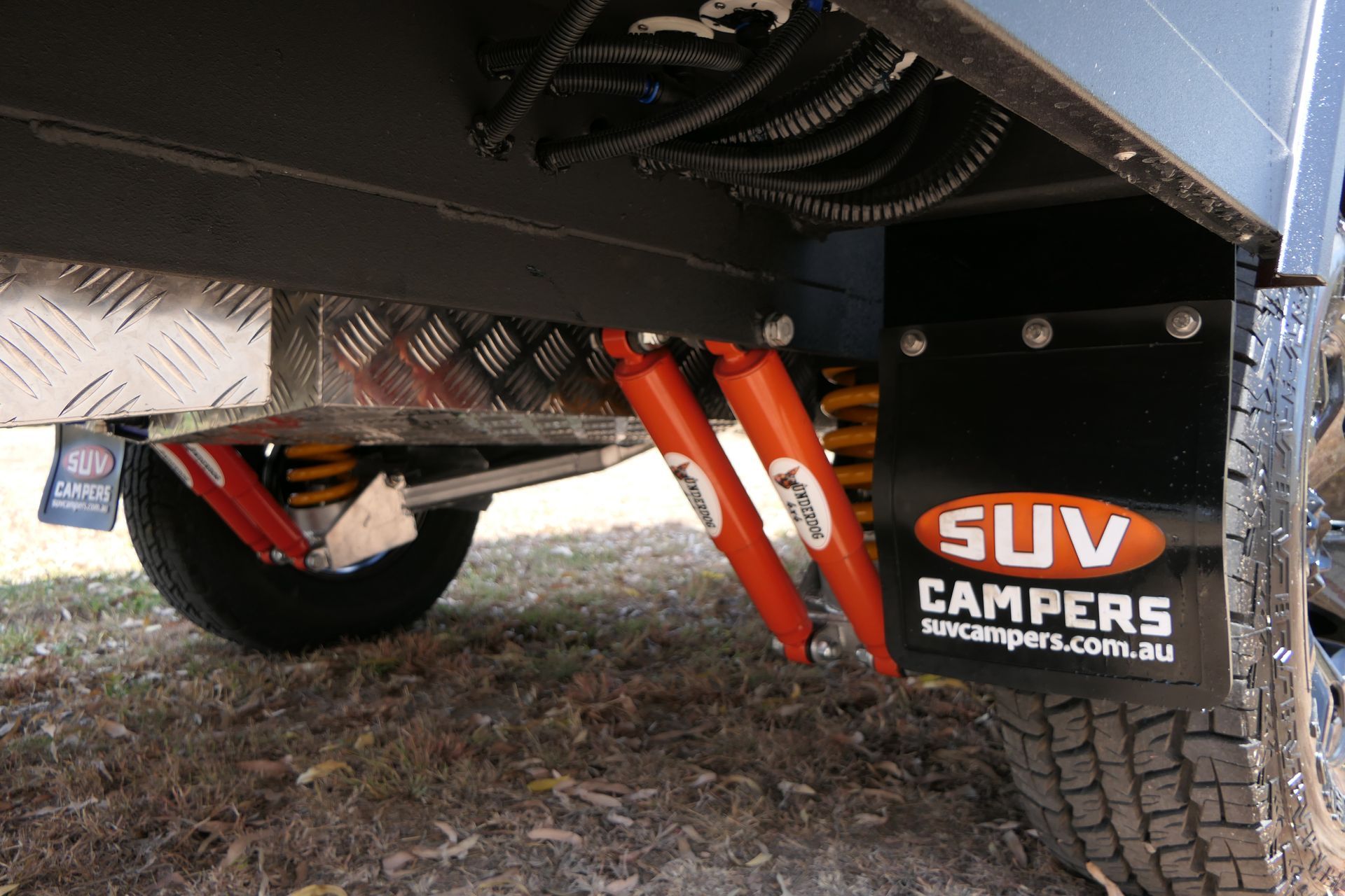 Underneath of an SUV Camper with orange shock absorbers, mud flaps and tire.