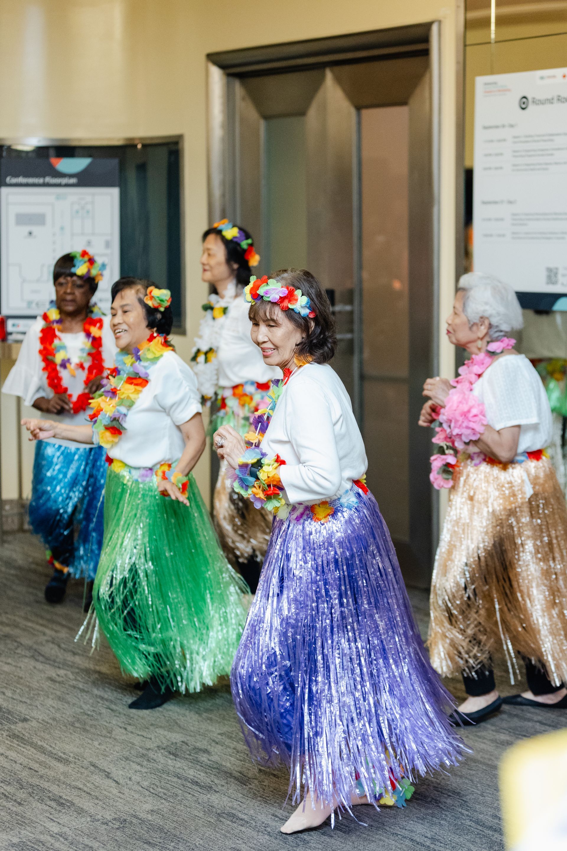 Un groupe de femmes âgées dansent le hula devant un ascenseur.