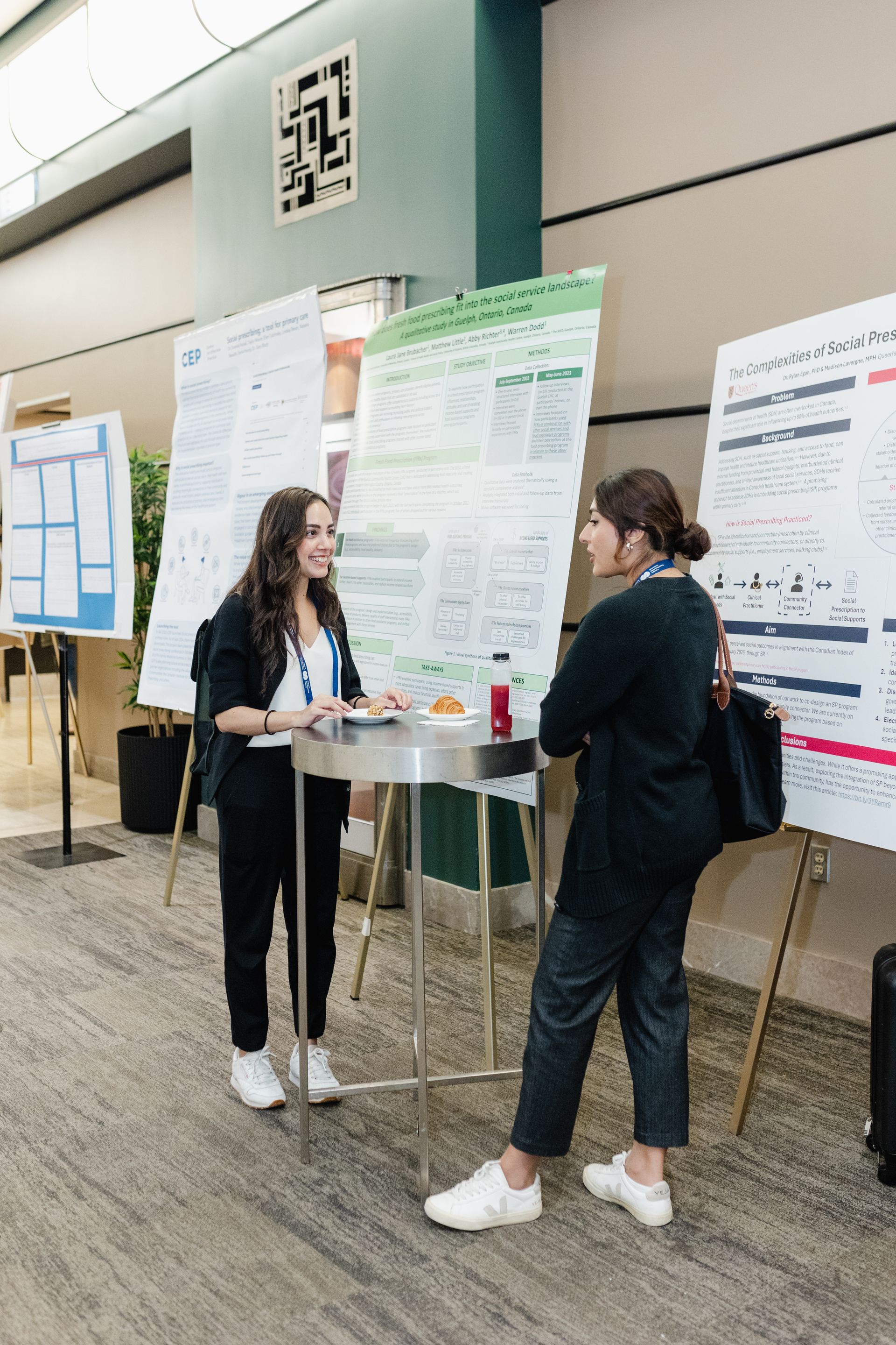 Deux femmes sont debout à une table et discutent entre elles devant des affiches.