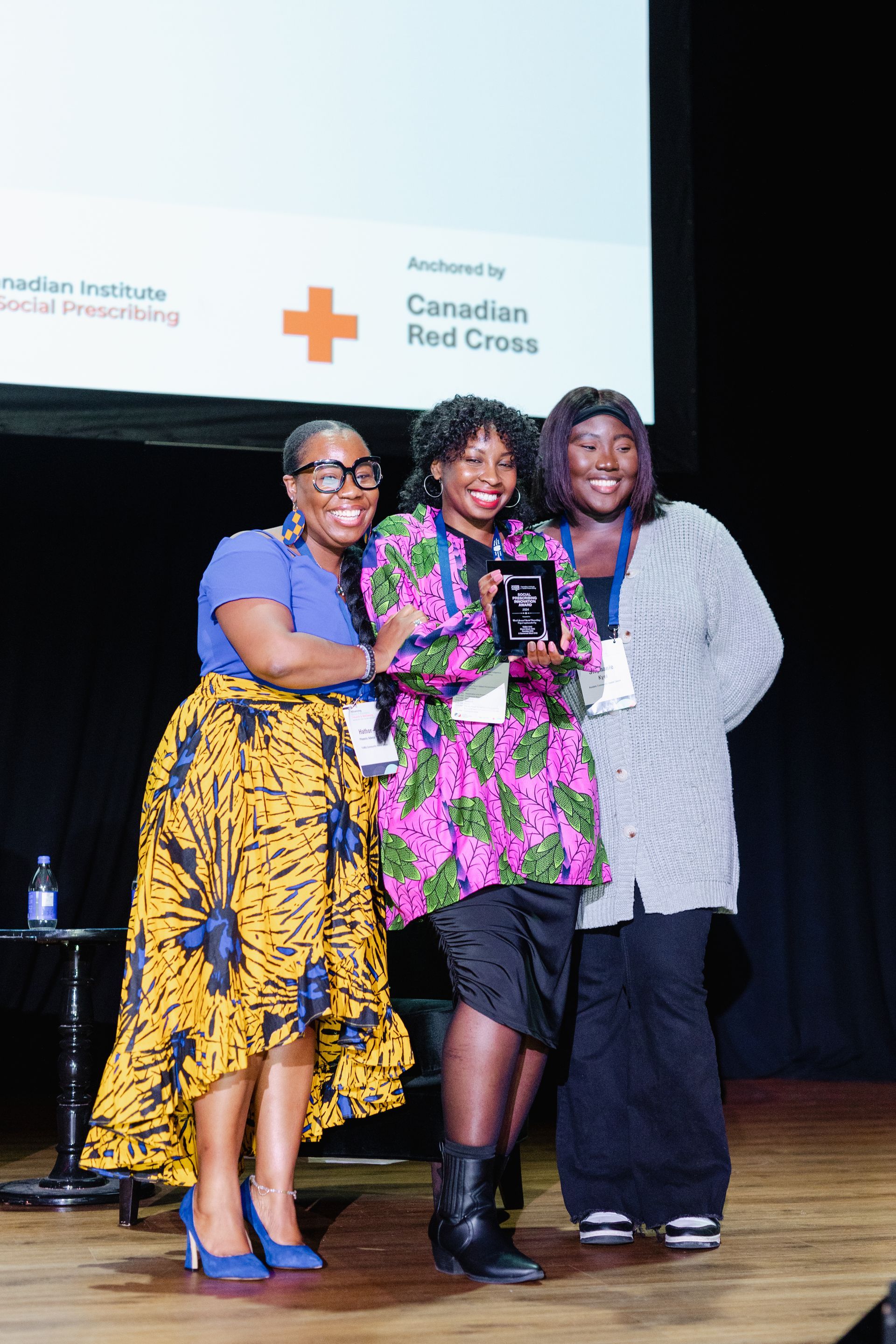 Trois femmes se tiennent côte à côte sur une scène, tenant un trophée.