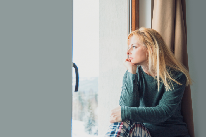 A woman is sitting on a window sill looking out the window.