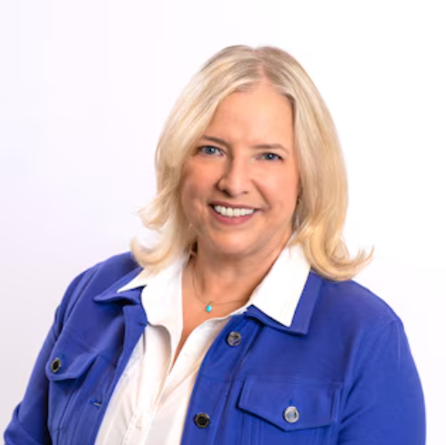 A woman wearing a blue jacket and white shirt is smiling for the camera.