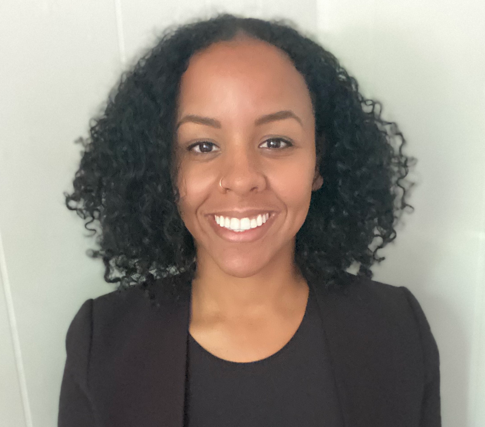 A woman with curly hair is smiling and wearing a black jacket.